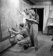 Staff officers plotting troop positions during the invasion of Sicily on a wall map in the underground operations room at Malta, 9 July 1943. NA4094