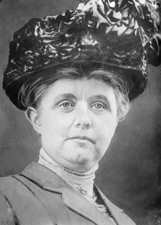 A black-and-white photograph of a woman wearing a large, decorative hat