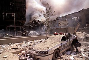 Rescue worker reaching into a New York Police car covered with debris (28802606564)