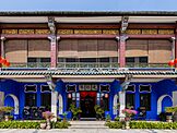 Front façade of a double-storey Oriental-style mansion, coloured in blue and with the upper floor partially concealed by wooden blinds.