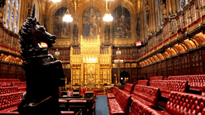 Wood-panelled room with high ceiling containing comfortable red padded benches and large gold throne.