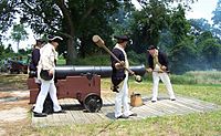People dressed in Revolutionary War military uniforms loading a cannon