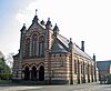 A chapel with rows of red and white bricks; the entrance porch has three arches and there are three windows above