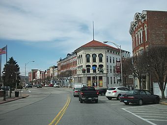 A view down a street with a signalized intersection, at red state with two cars waiting for it to change, in the foreground. It curves off to the left; on the right are old-fashioned buildings and low, bare trees.