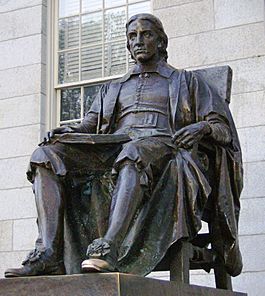 A bronze sculpture, on a tall granite plinth, of a man sitting in a chair with an open book in his lap. The statue as a whole is darkly weathered, but the toe of the figure's left shoe is shiny as if from frequent rubbing.