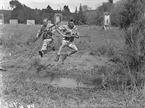 Two airmen leap over a ditch with rifles