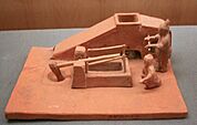 Small ceramic model of two men operating a tilt hammer and winnowing machine