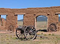 Old wagon wheels in front of a ruined clay wall with arched opening and windows
