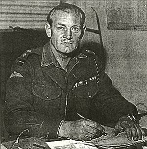 Black-and-white photograph of Churchill in uniform, sitting at a desk, and looking up at the camera while writing