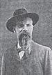 Head and torso of a white man with a long goatee, wearing a wide-brimmed hat, bow tie, and dark suit coat.