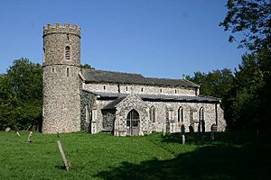 A flint church seen from the southeast; on the left is a round tower with a battlemented parapet, and the body of the church, with a porch and a small clerestory, extends to the right