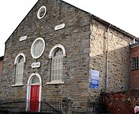 Symmetric stone-faced front of a small chapel with a round window above a red door and two windows to either side