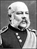 Head and shoulders of a balding white man with wide sideburns connecting to a mustache. He is wearing a military jacket with shoulderboards and a wide sash across the chest.