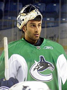 An ice hockey goaltender with his mask pulled off of his face looking forwards. He wears a green jersey with a logo of a stylized orca in the shape of a "C".