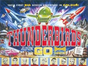 A bold title in the centre of the image reads "Thunderbirds Are Go". A top caption spanning the width of this colourful film poster reads "Their First Big-Screen Adventure In Colour!" Between the title and the caption, three rocket-shaped vehicles – one blue, one green and one red – appear to blast outwards from the poster itself. Other images lining the sides of the poster include an exotic pink car, a snake-like rock creature apparently shooting fire from its mouth and, at the base, portraits of some of the principal cast members, who are marionette puppets.