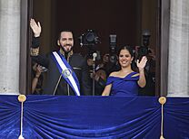 Nayib Bukele and Gabriela Rodríguez de Bukele standing at a balcony and waving to a crowd