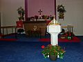 A Protestant church altar and font, decorated for Pentecost with red flowering plants and green birch branches
