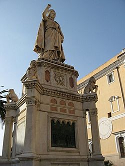 Oristano: Statue of Eleanor of Arborea, holding the Carta de Logu in her hand, with the sundial on the wall of the City Hall in the backdrop.