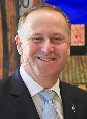 Head and shoulders of John Key smiling in a dark suit and pale blue spotted tie