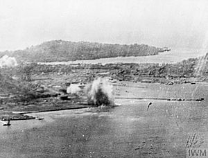 Black and white aerial photo of shoreline with smoke rising from buildings in the centre of the image