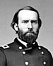 Head and shoulders of a white man with a full beard, wearing a double-breasted military jacket with a rectangular patch over each shoulder.