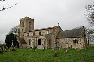 A stone and brick church seen from the southeast showing, from the far end, a battlemented tower, a nave with clerestory, aisle and porch, and a smaller chancel