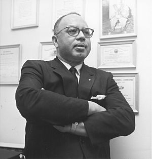 Man wearing suit and glasses, standing with arms crossed