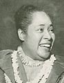 A smiling woman with a topknot and strings of shells around her neck