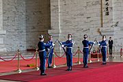 Five men in blue uniforms and silver helmets performing a rifle drill