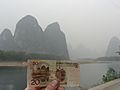 A hand holding up a Chinese yuan bill next to the location that is depicted on the bill