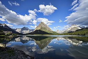 Photos of a very still Swiftcurrent lake with clouds, trees, and mountains reflecting in the water like a mirror.