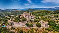 Aerial view of a ruined hilltop château and chapel surrounded by trees and rolling hills in Provence, France.