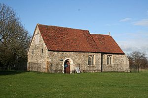A small, simple stone church with a red tiled roof. On the left is the nave with a round-headed doorway, and to the right is the smaller chancel