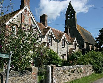 A row of cottages, partially obscured by vegetation. In the background is the bell tower of a much large building.
