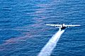 A large four propeller airplane sprays Corexit onto oil-sheen water