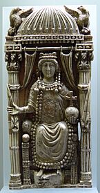 A carving of a crowned woman seated on a throne behind undrawn curtains. She is holding a cross atop a globe on her left hand