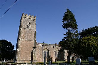 Stone building with square three stage tower at the left hand end. Trees to the right hand gravestones in front.