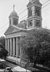 Black-and-white photograph of a large church with a portico; two twin bell towers extend from both sides of the building.