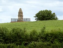 Stone obelisk surrounded by railings set in green fields and trees
