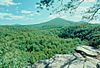 View from a flat rock across a forest to several wooded mountain peaks