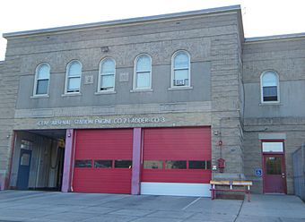 A two-story beige brick building with three garages at street level. Two have their red doors closed. Above them are metallic letters spelling out "Clay Arsenal Station Engine Co. No. 2 Ladder Co. No. 3". On the second story are five round-arched windows.