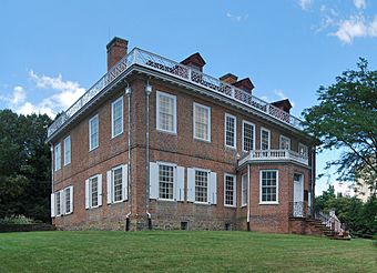 A two-story brick house with white window shutters, a wooden balustrade on top and an octagonal projecting front entrance pavilion, seen looking slightly upslope towards its right corner