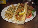 An alligator po' boy sandwich, with French fries and vegetable garnish