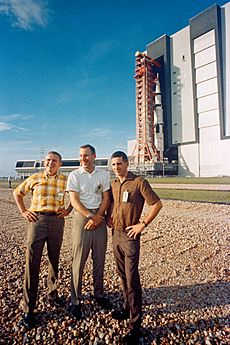 The Apollo 8 prime crew stands in foreground as the Apollo space vehicle