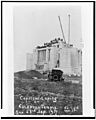 The Cardston temple at a distance, as if on a postcard. People can be seen at a distance standing on top of the structure, an old car sits in the middle of the shot, sitting on a hill, among other hills of dirt. 