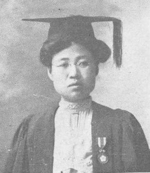 A young Asian woman wearing a mortar board and academic gown, with a medal pinned to the gown. Her dark hair is dressed up and slightly puffed under the mortar board.