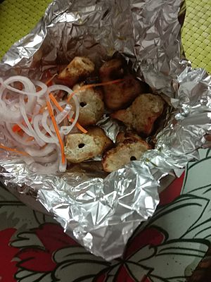 Reshmi kabab served on foil sheet and accompanied by salads.