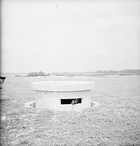 The turret of a Pickett-Hamilton retractable fort, fully raised and manned by a Bren-gun team of the Coldstream Guards, taken on a fighter airfield in Southern England.