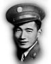 Head of a smiling young man wearing a peaked cap with a round medallion on the front and a military jacket over a shirt and tie.