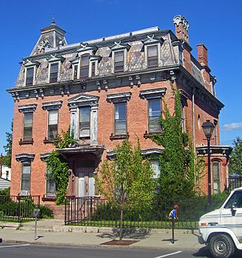 A brick house with a slate tiled roof and short green trees in front